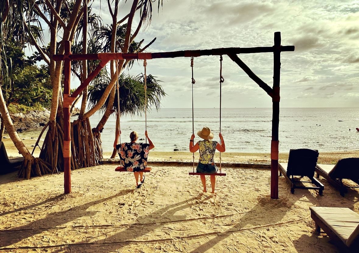 Two travellers on beach swings looking out to the Andaman Sea at golden hour