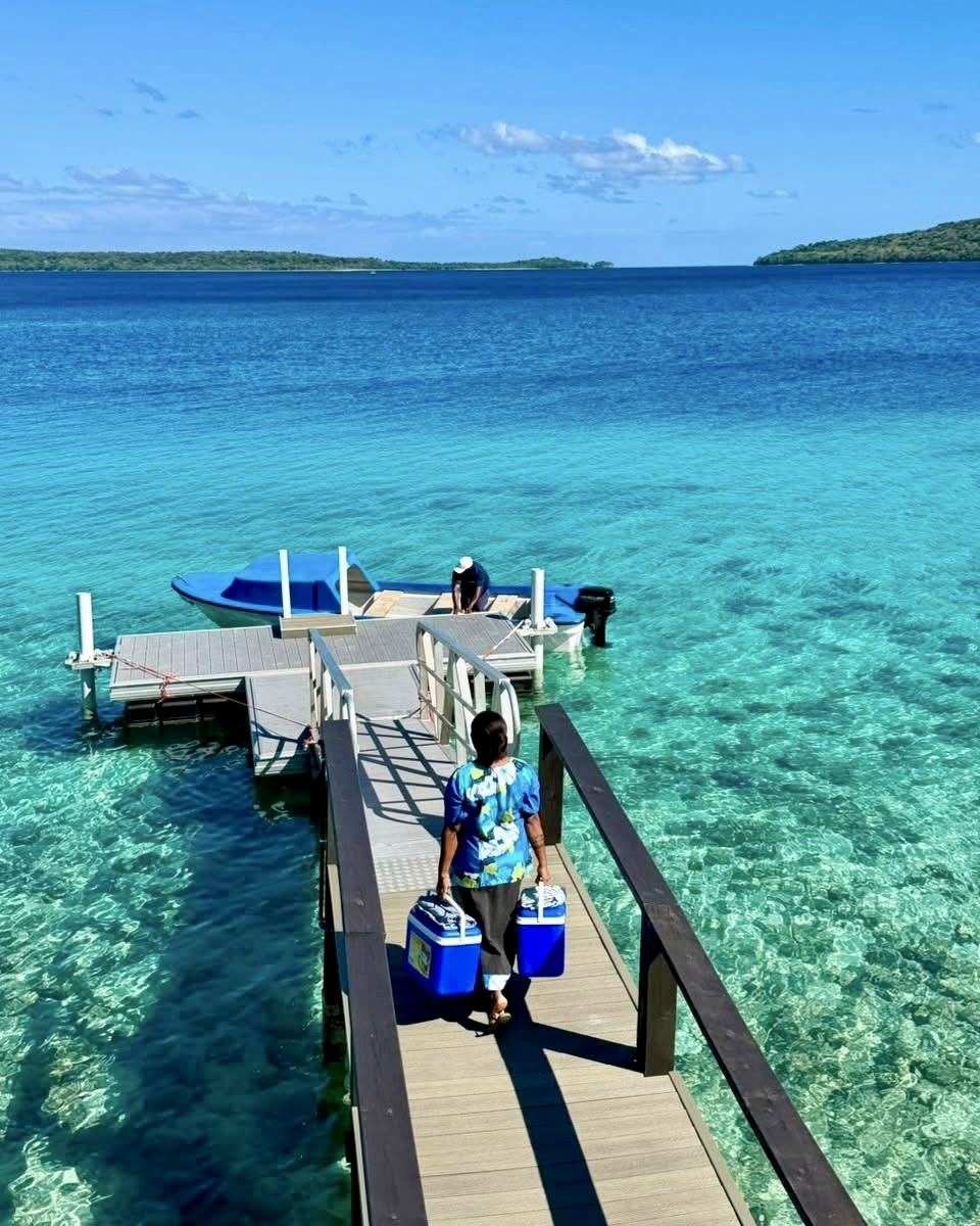 Resort staff carrying supplies along a jetty above clear turquoise water in Vanuatu