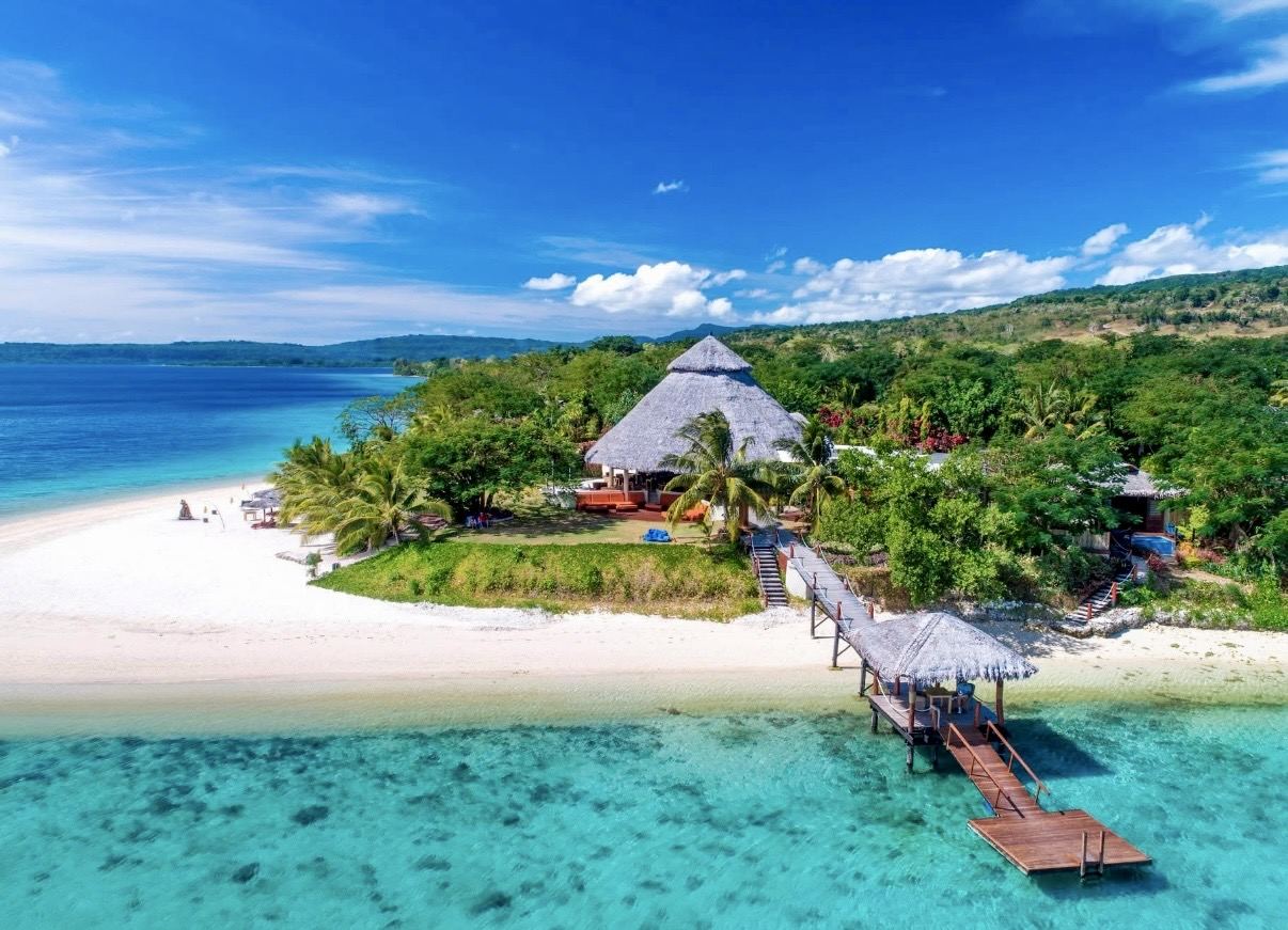 Aerial view of a thatched island resort, white beach and jetty over a turquoise lagoon in Vanuatu