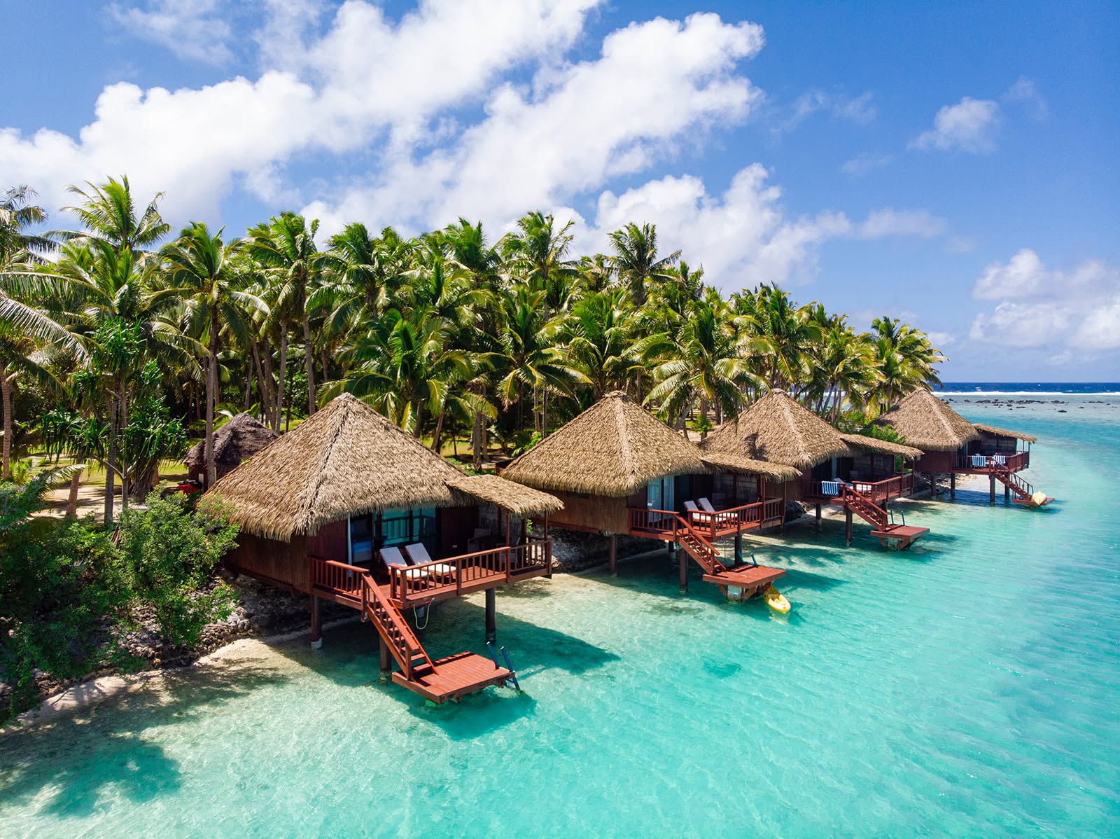 Thatched overwater bungalows above a clear turquoise Cook Islands lagoon