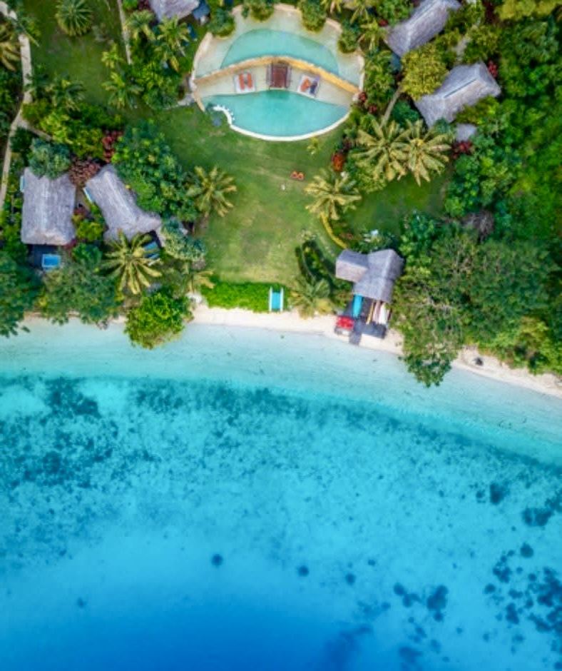 Overhead view of a Vanuatu resort pool, thatched bures and reef-fringed beach