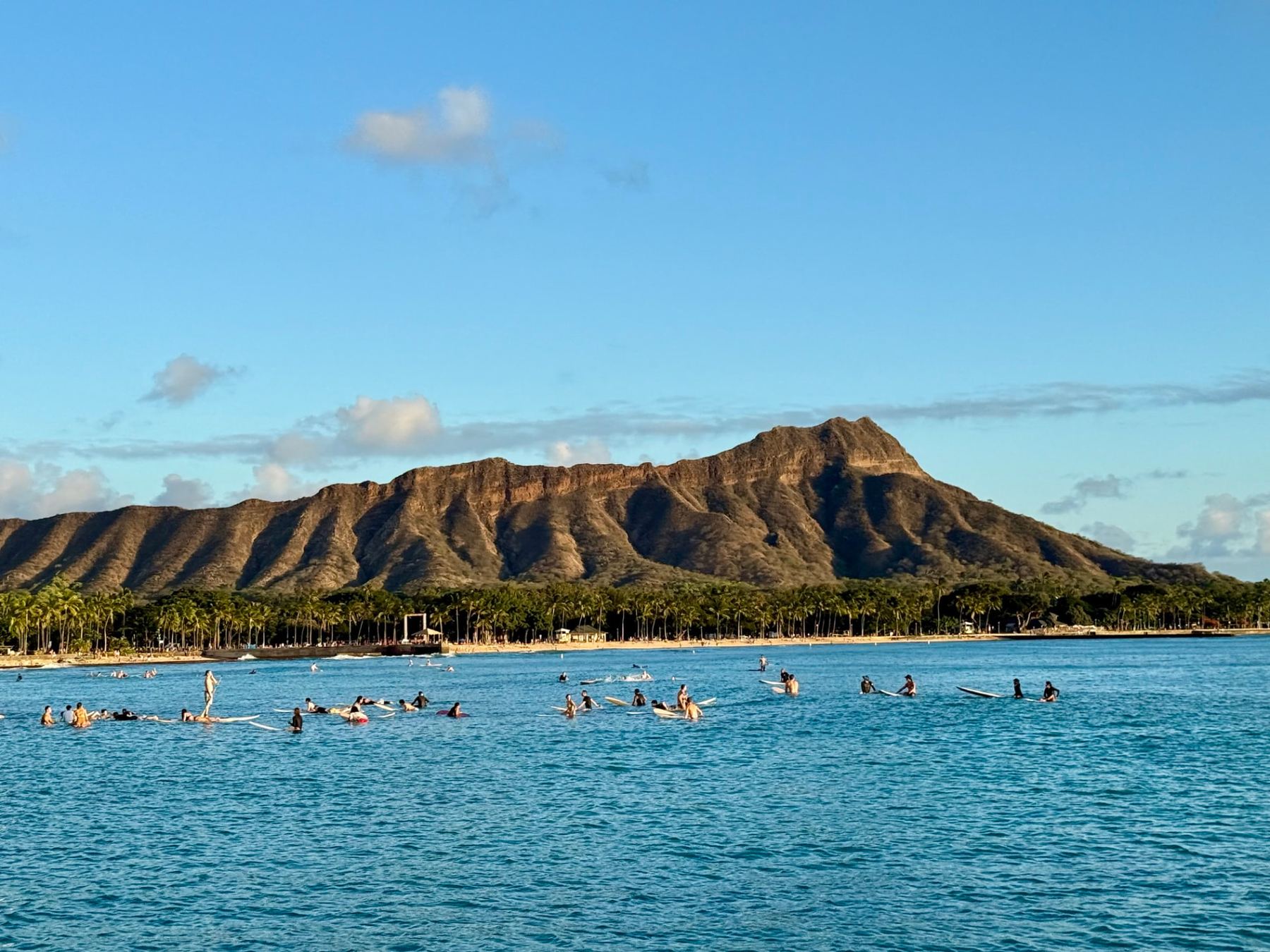 Diamond Head rising above surfers in the water off Waikiki, Oahu