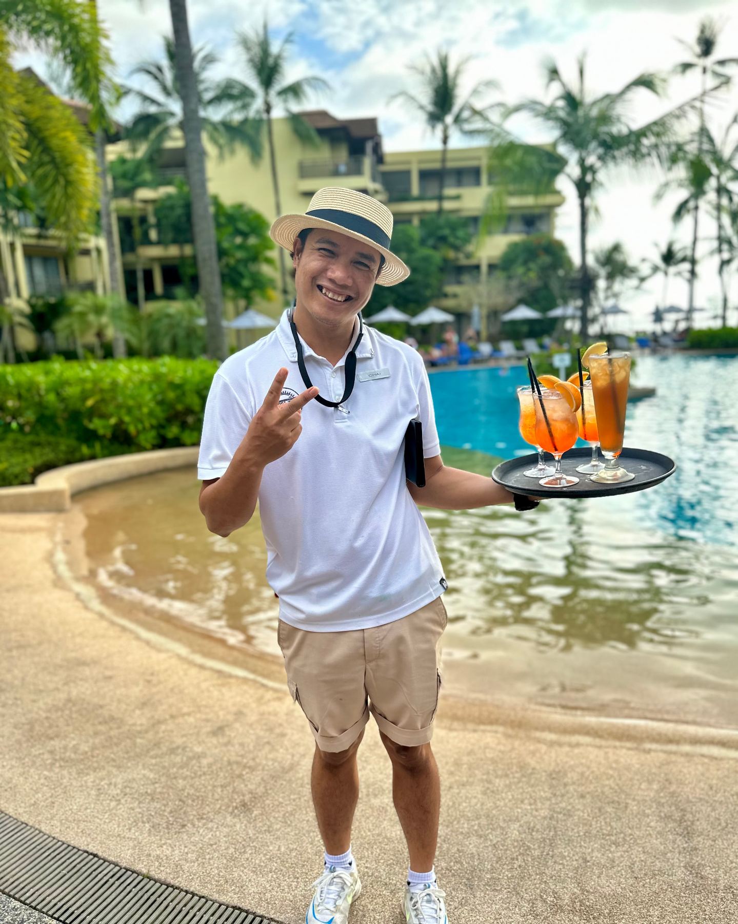 Smiling resort waiter carrying cocktails beside a palm-fringed pool in Thailand